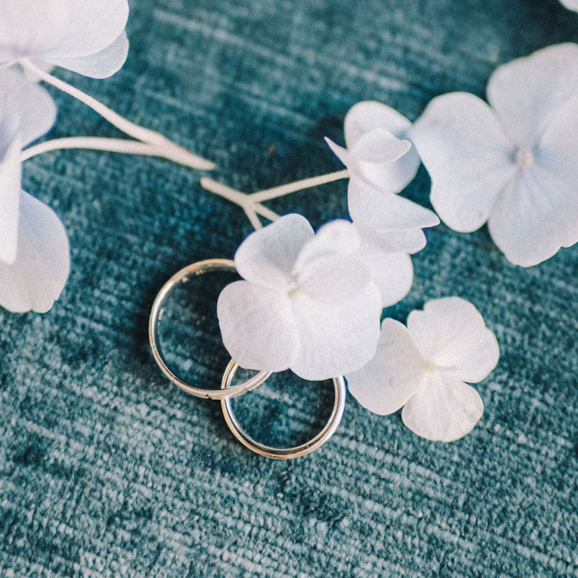 Two wedding rings on a blue cloth with white flowers at the Pennsylvania bridal shows.