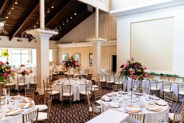 Elegant banquet hall with round tables set for dining, decorated with floral centerpieces and gold chairs, under a high ceiling with exposed beams—perfect for hosting events like the Gettysburg Wedding Expo.