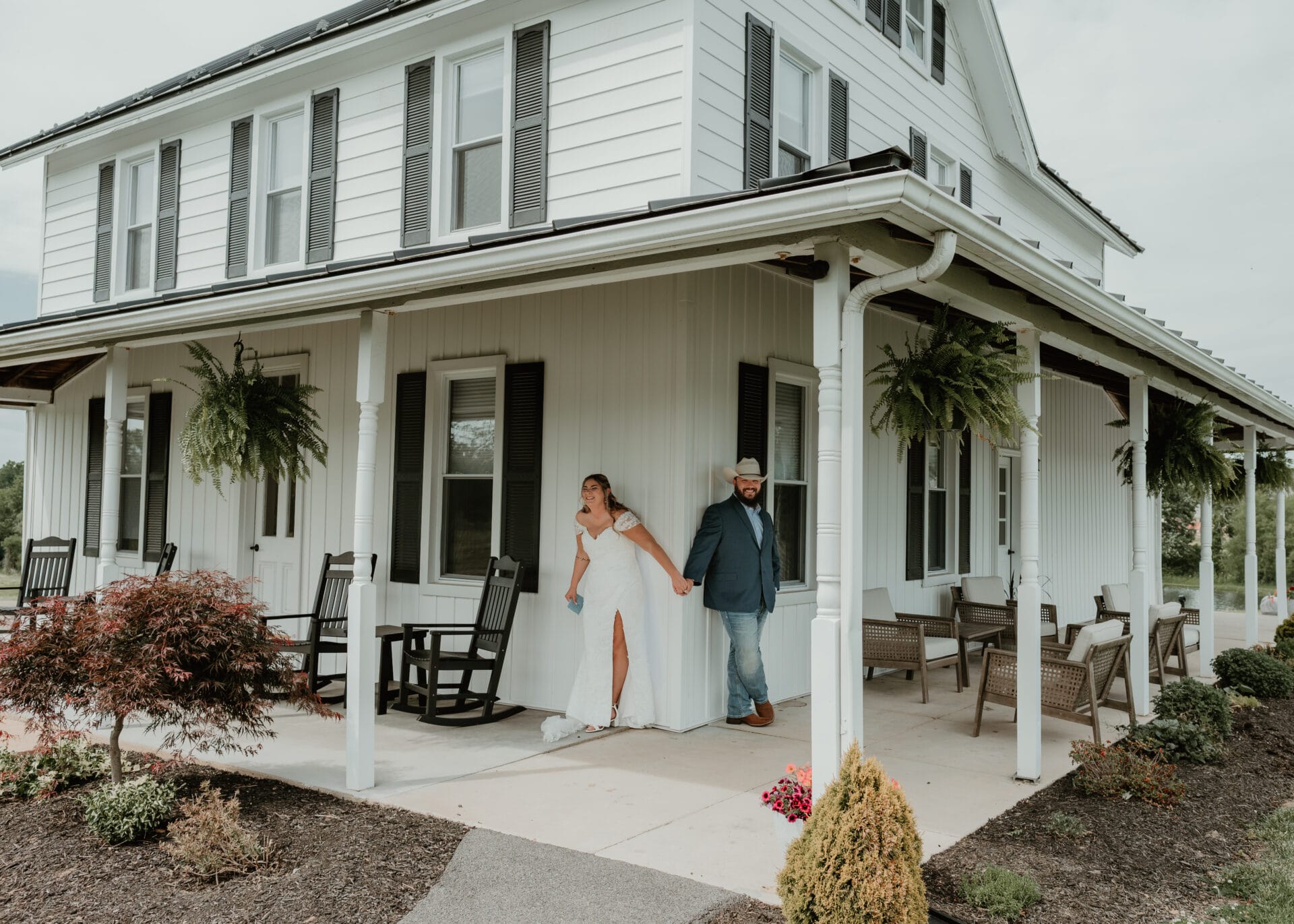 Bride and groom stand outside farmhouse.