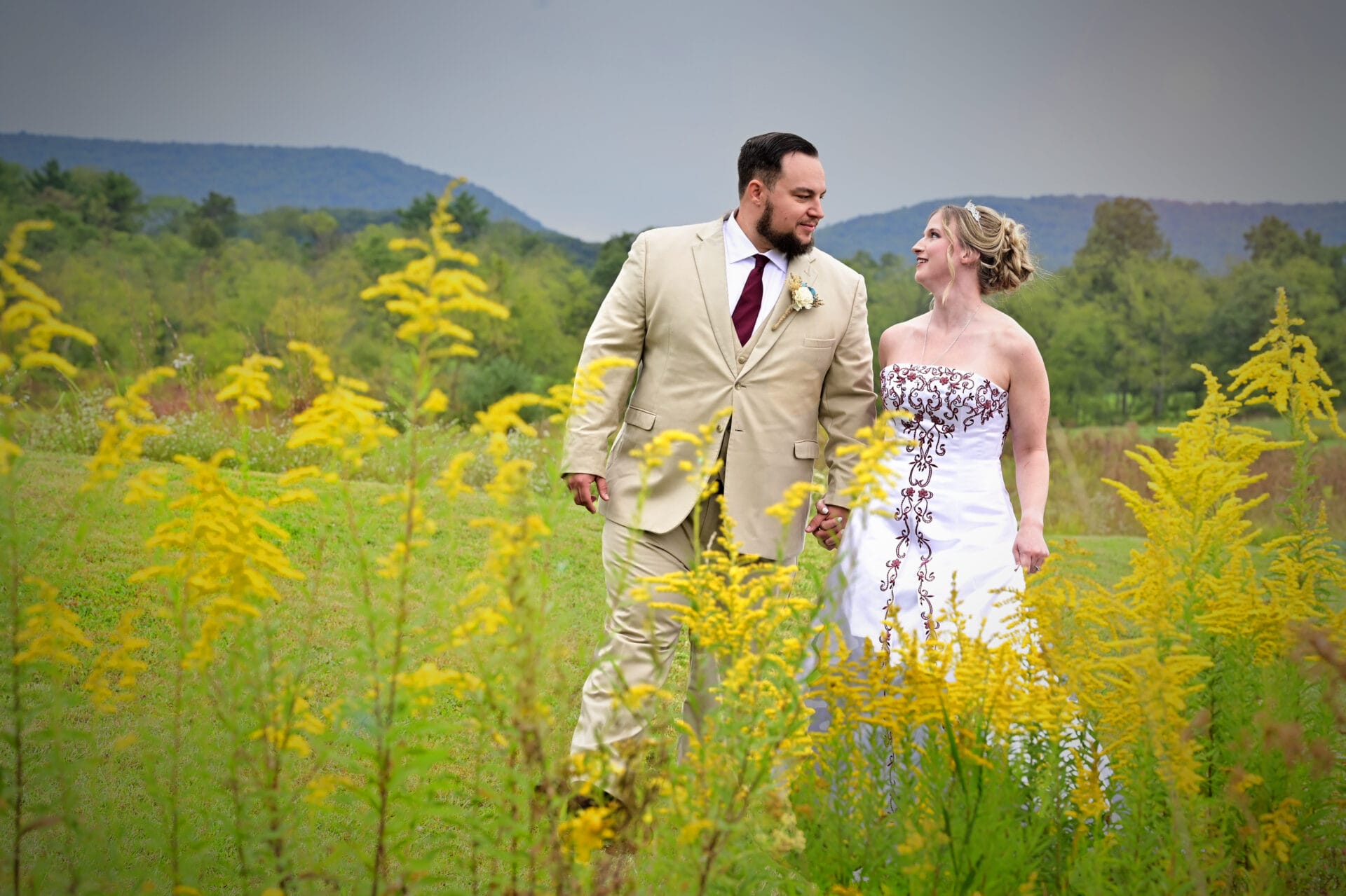 Couple stands in field of yellow flowers on wedding day.
