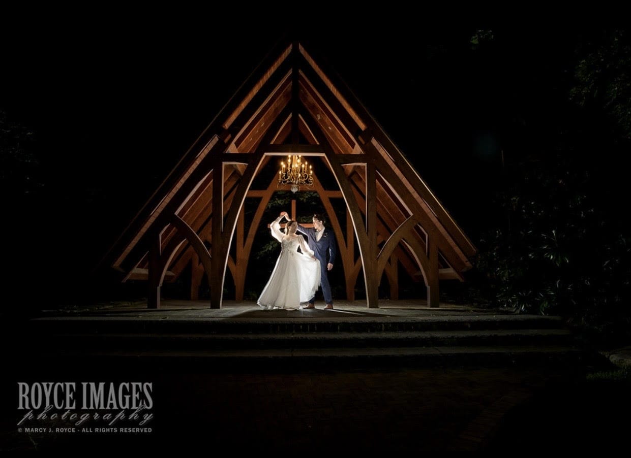 Bride and groom dancing under arch in dramatic lighting.