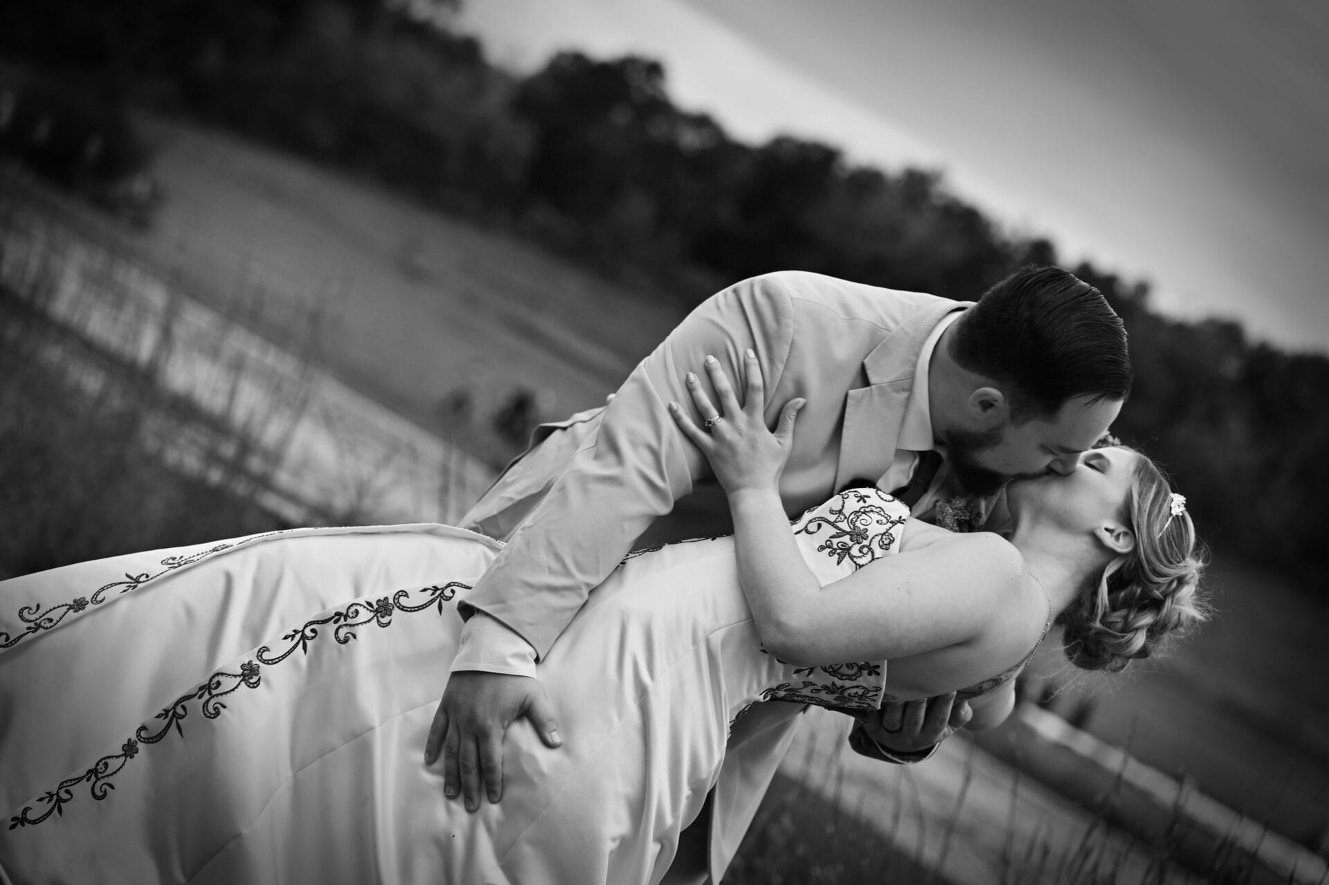 Husband dipping wife in kiss in black and white photo.